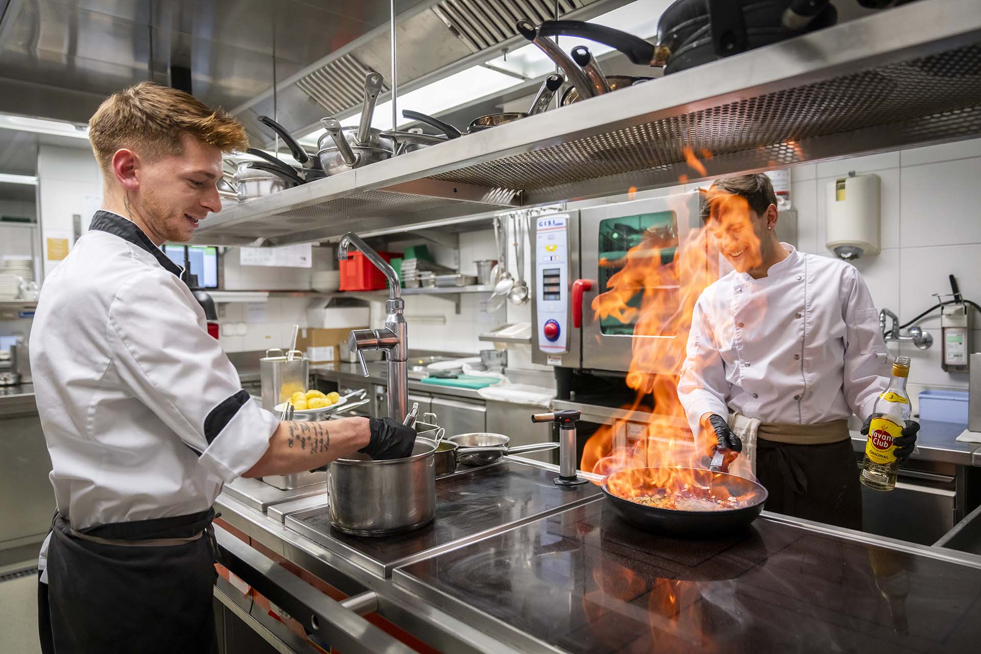 In der Kueche des Hotel Lenzerhorn flambiert ein Koch ein Gericht in der Pfanne, waehrend sein Kollege im Topf ruehrt