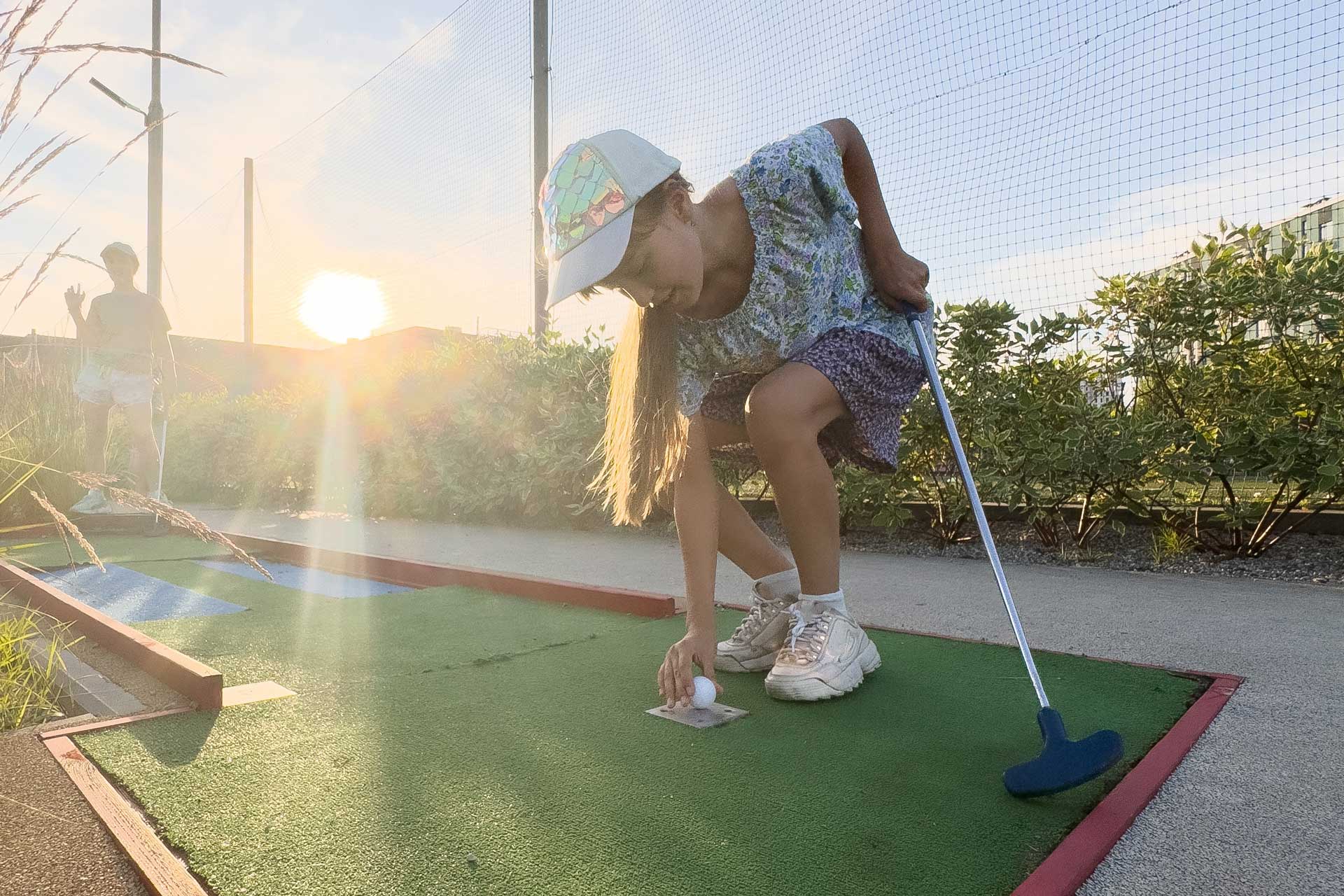 Ein Kind spiel Minigolf und hebt gerade den Ball auf